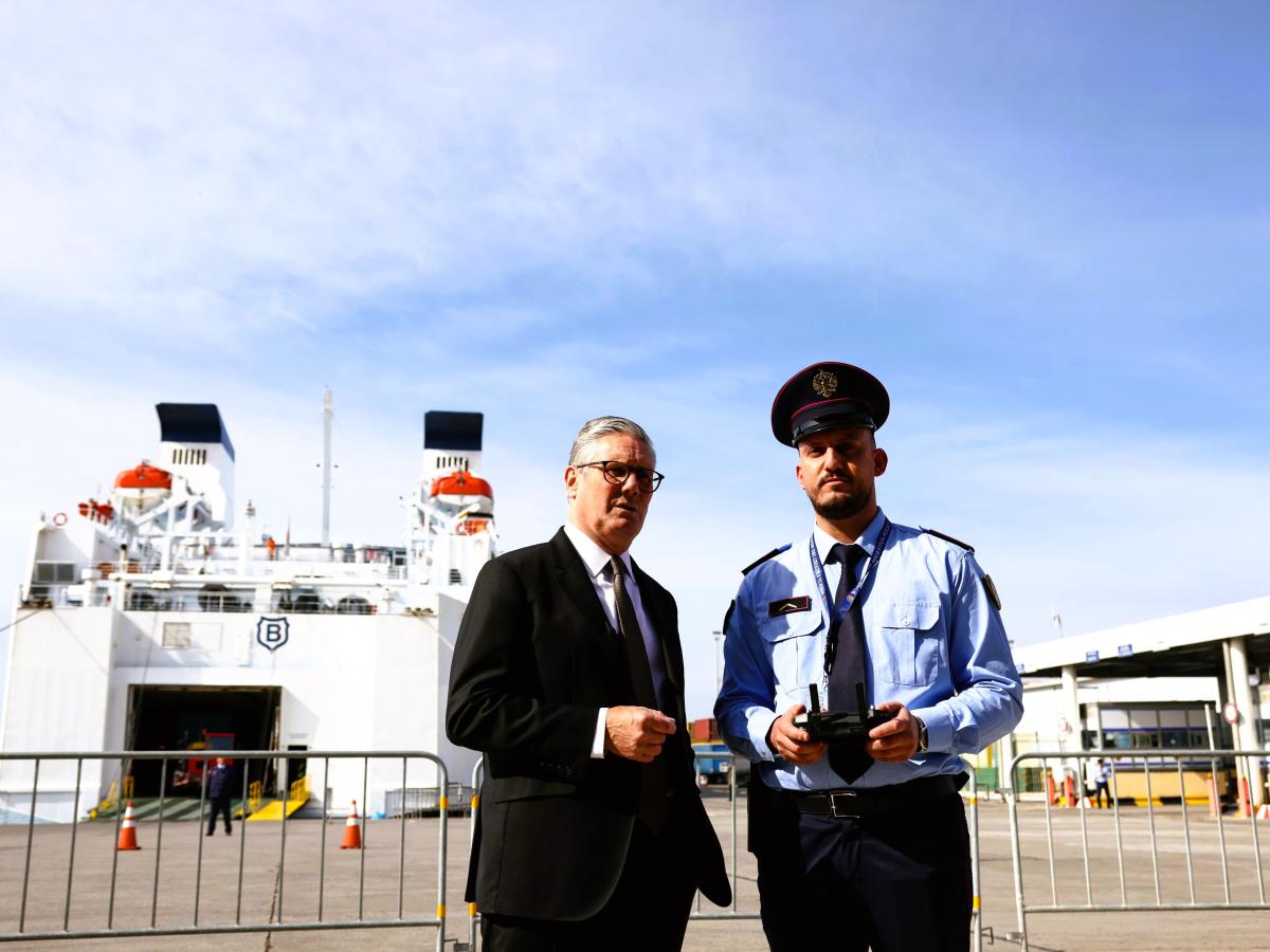 A prime minister stands next to an Albanian police officer in front of a ferry.