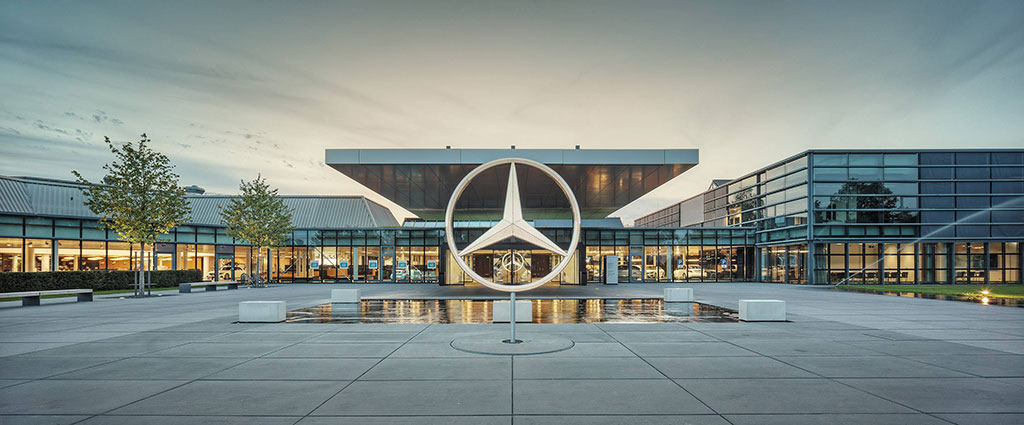 A large sculpture of the Mercedes Benz three-point star stands in front of a large, low glass fronted showroom.