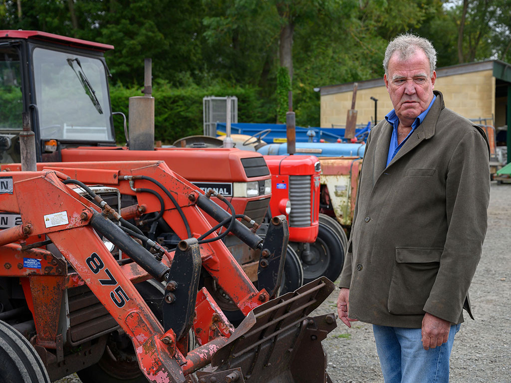 A man stands looking baleful next to a row of red tractors