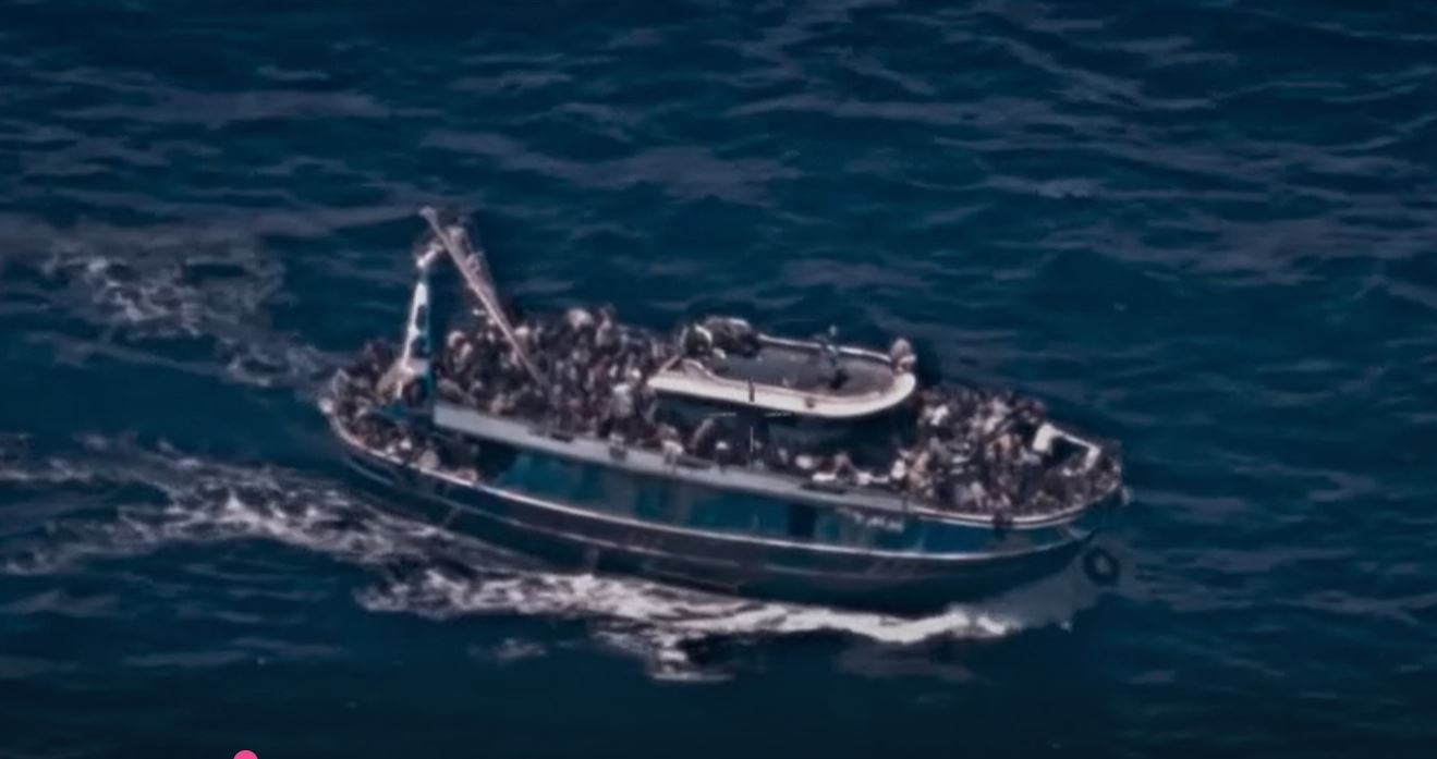 A grainy surveillance picture of an rusty boat overloaded with people