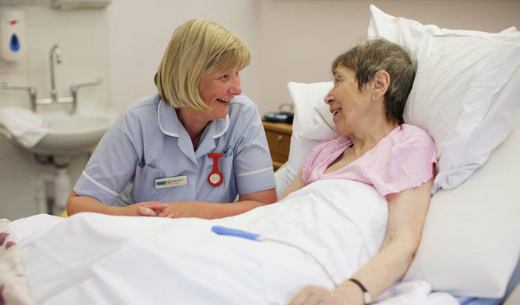 A nurse bends beside a bed and talks to a patient