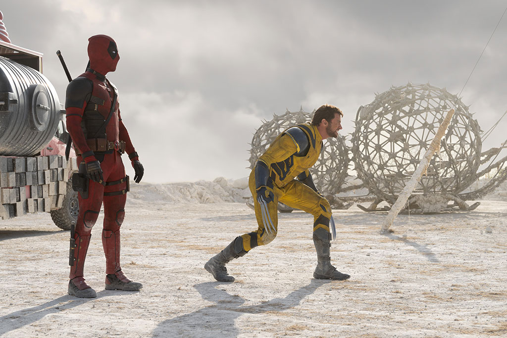 Two superheroes, deadpool and Wolverine, stand and crouch respectively, in a desert like place.