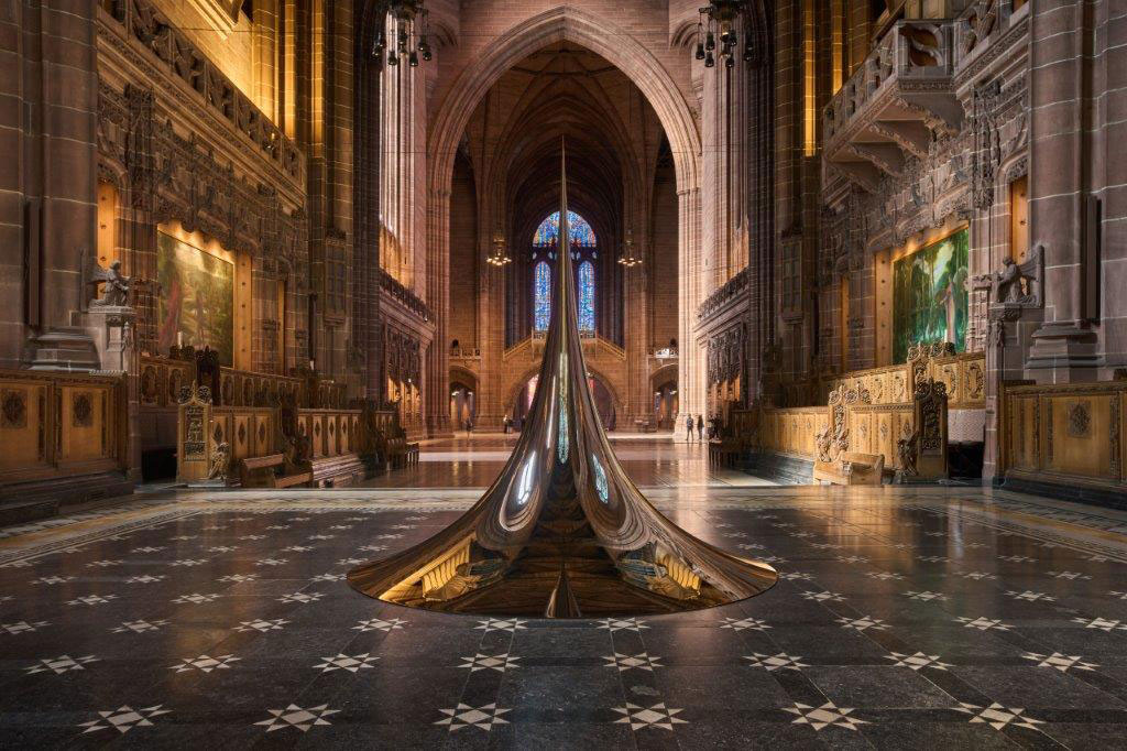 An art structure of a circular peak sits on the chequered floor of a cathedral.