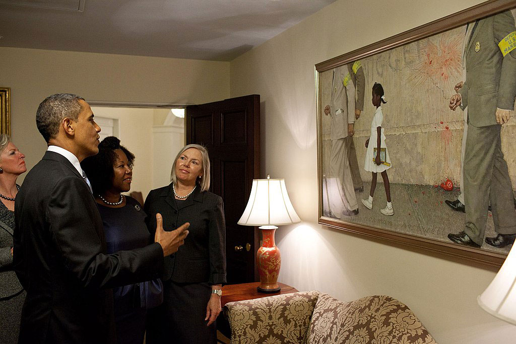 Barack Obama and a middle aged black woman look at a picture of her when she was a child walking between guards protecting her.