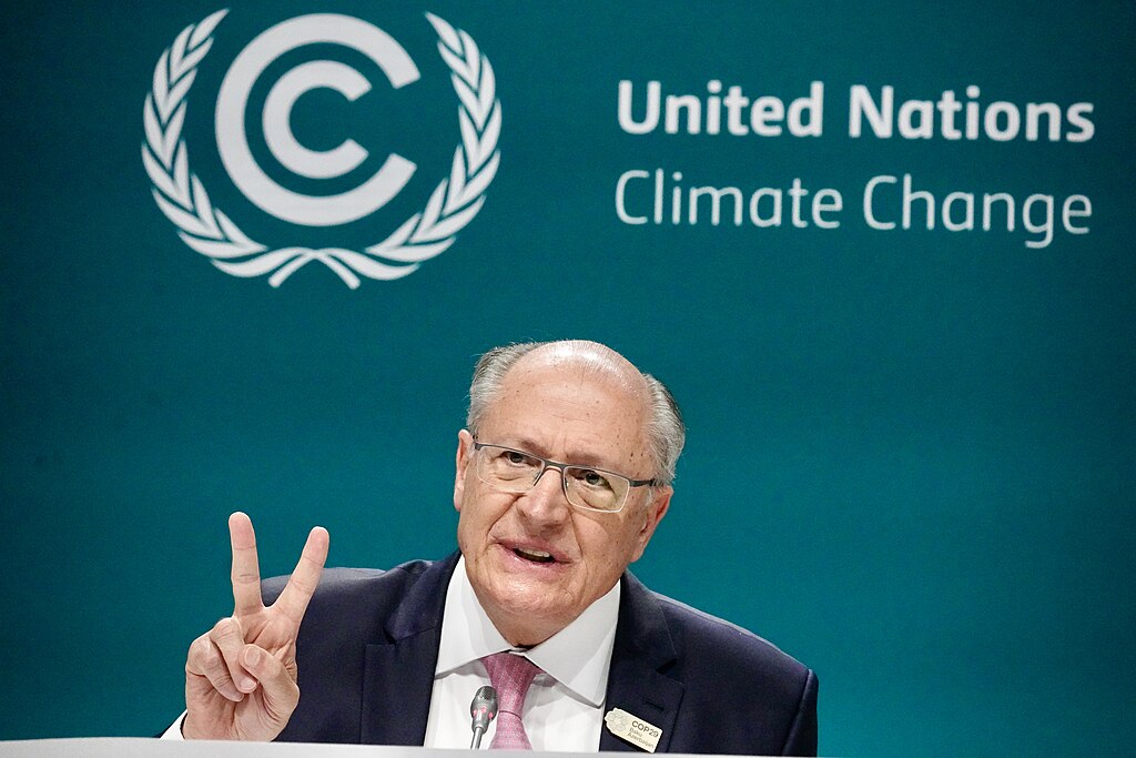 A speaker holds two fingers up while sitting in front of a backdrop reading 'United Nations Climate Change.