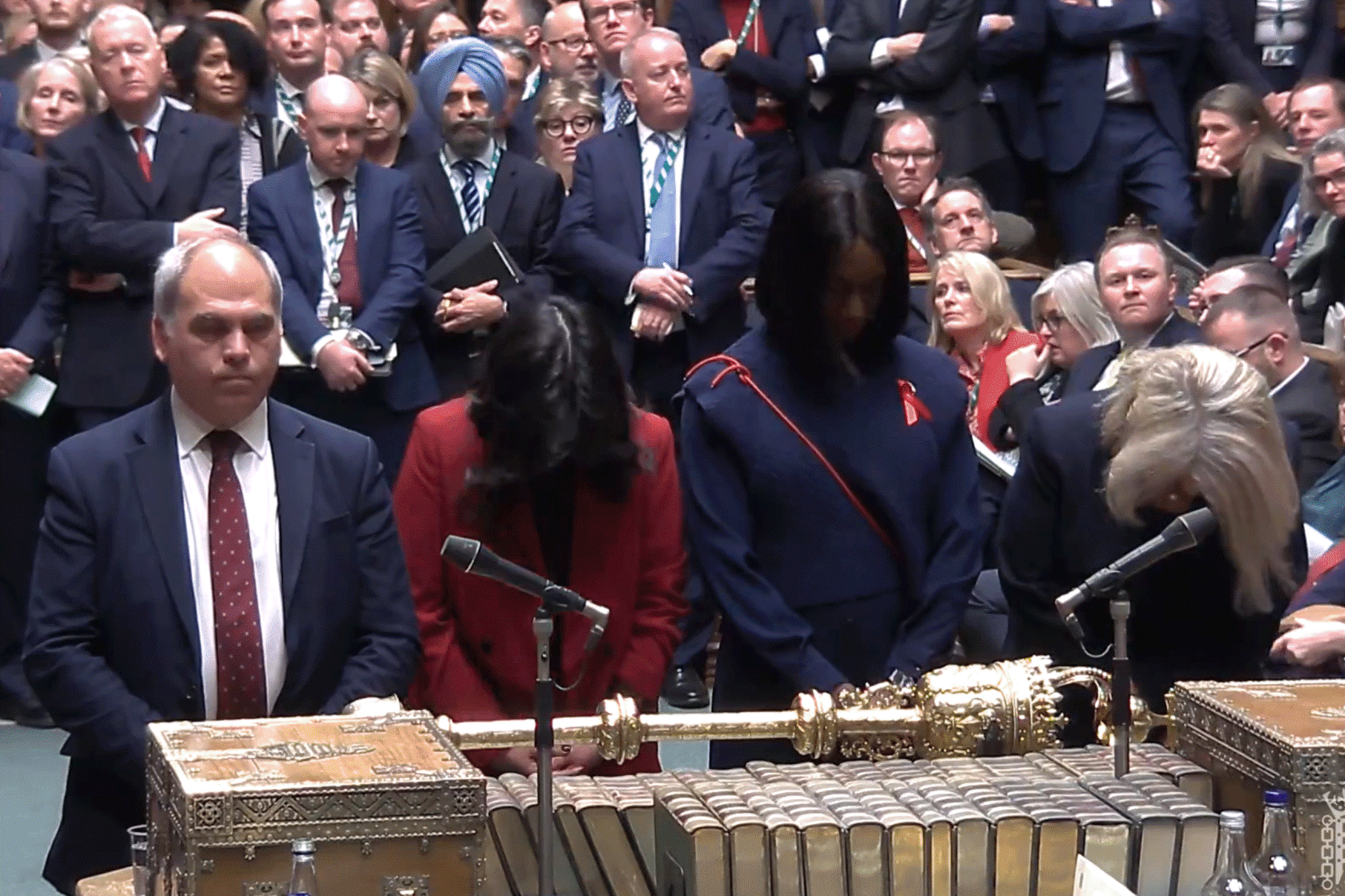 Four MPs stand at a table with heads bowed.