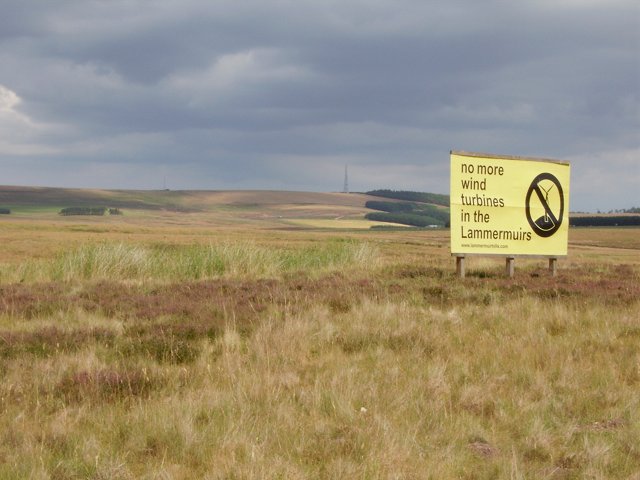 A sign protesting a proposed wind farm stands on flat moorland.