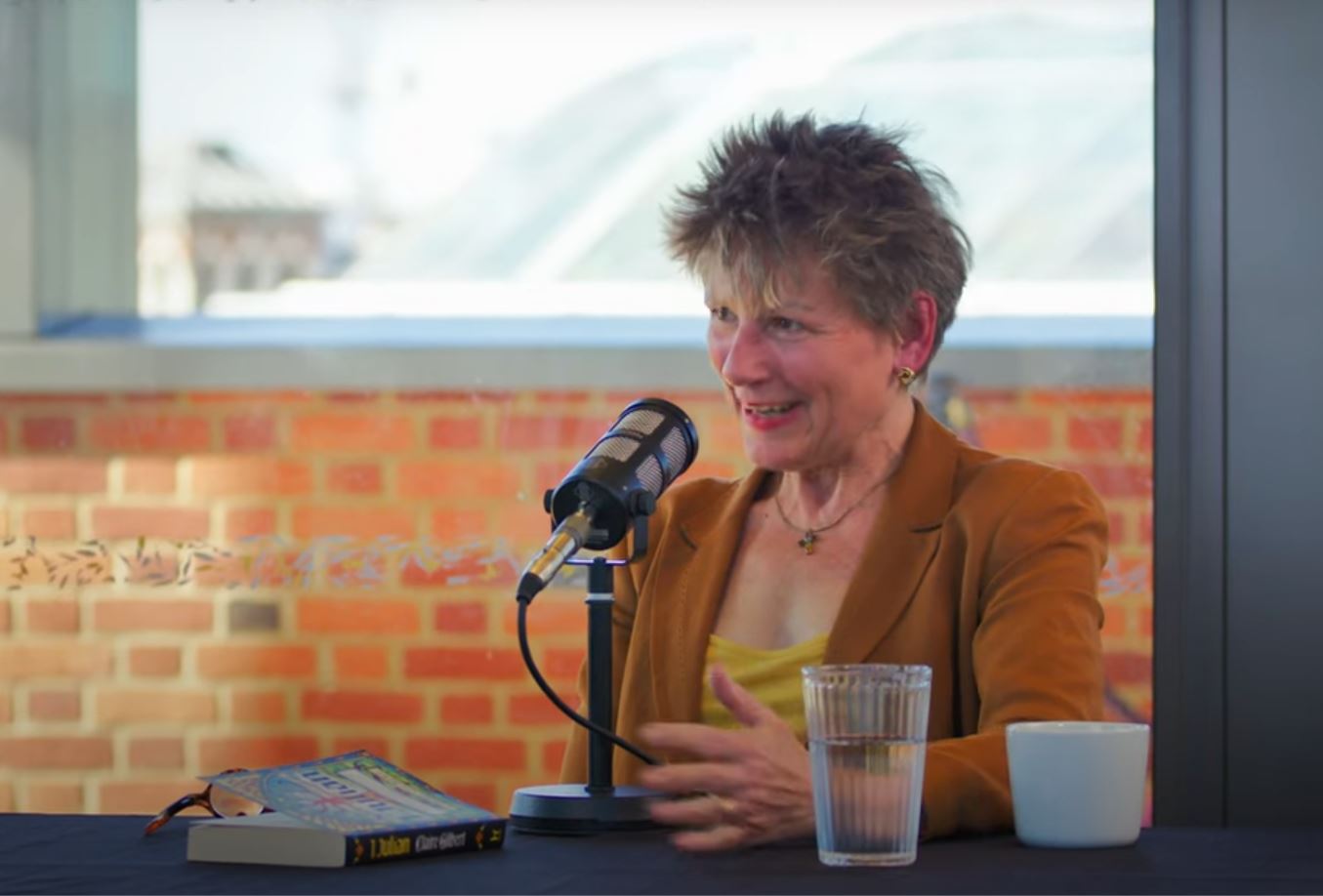 A woman sitting at a table in front of a microphone talks and gestures