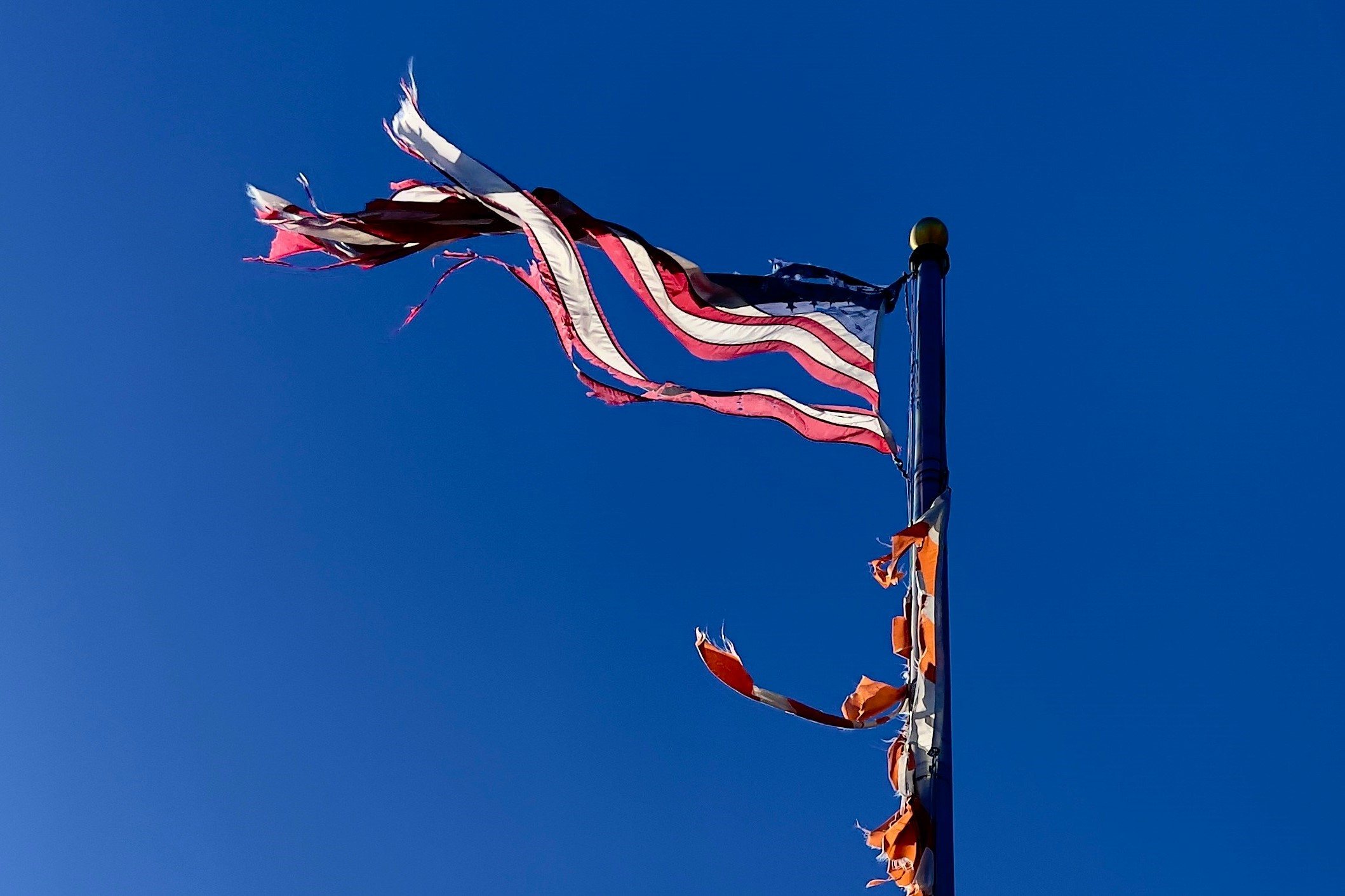 a tattered American flag flies against a blue sky.