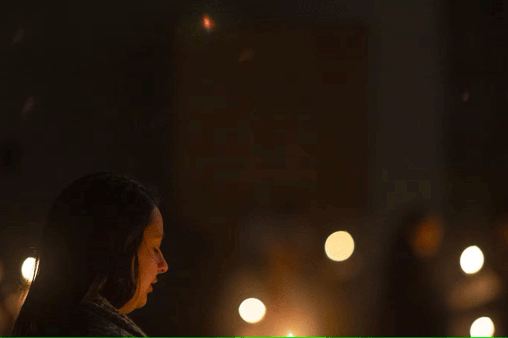 A carol singer looks down while candles flicker.