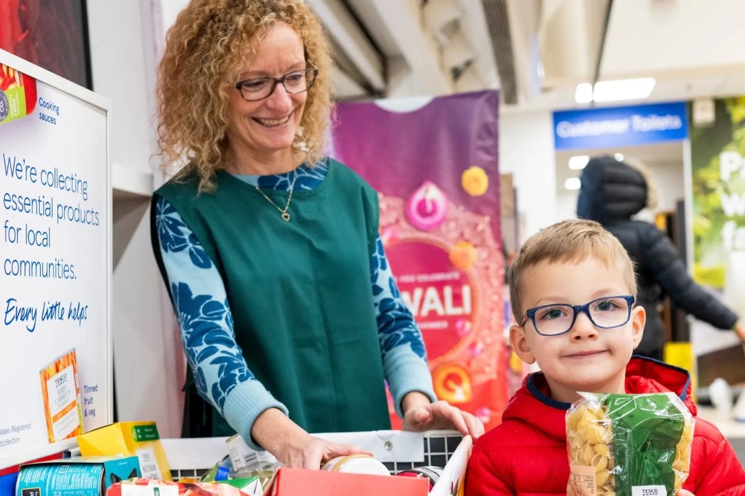 A shop assistant stands by a foobank trolley, while a child holds a packet of pasta beside it