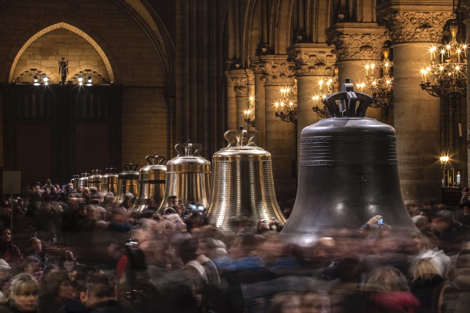 Restored church bells lined up in a cathedral, as crowds mill around them.