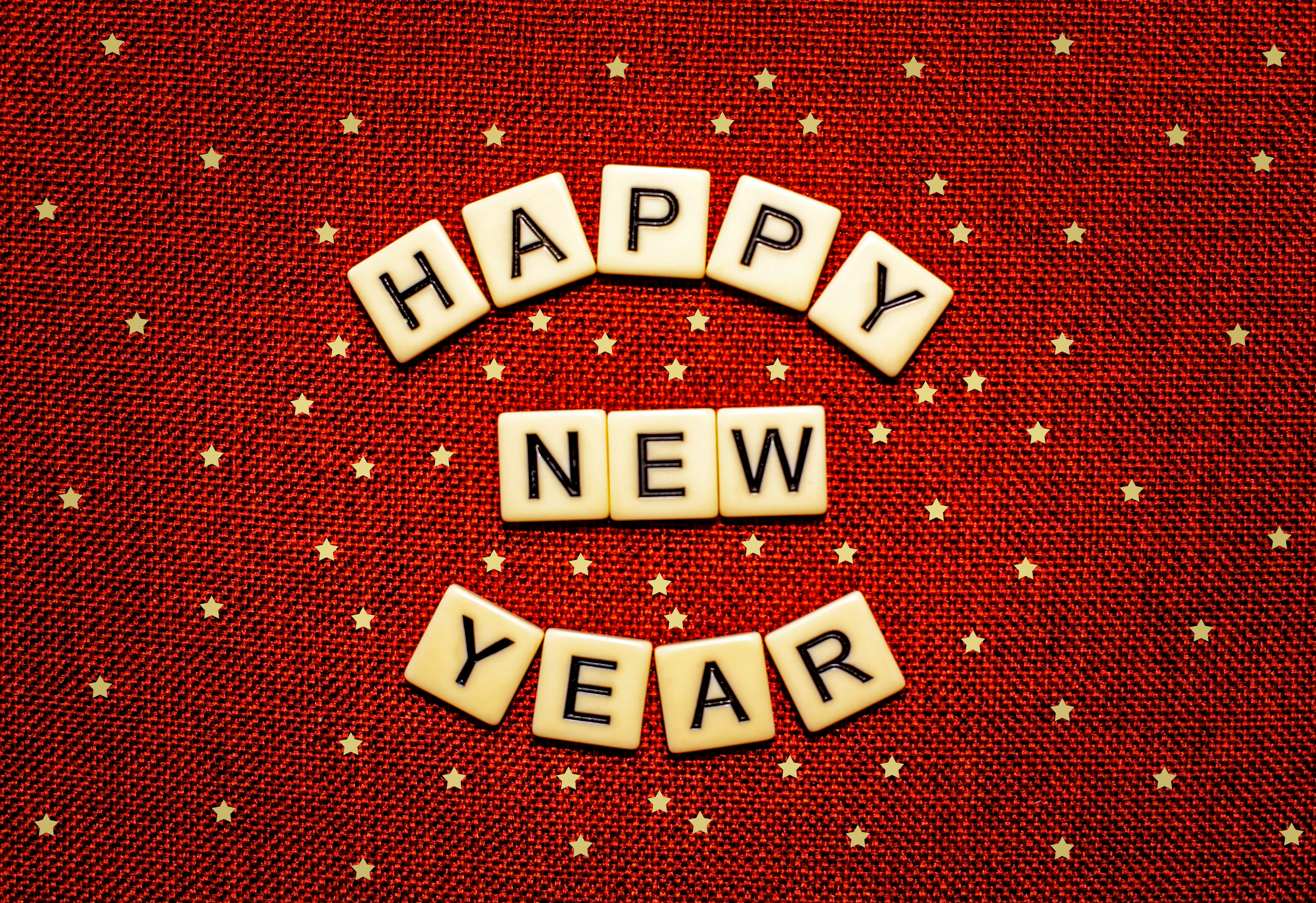 Scrabble letters read 'Happy New Year' against a red starry background.