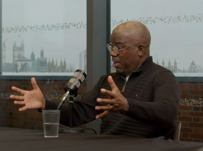 A podcast guest talks in front of a mic, while gesturing with both hands.