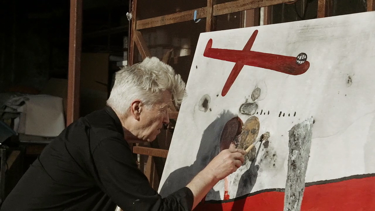 A man paints a canvas with red images.