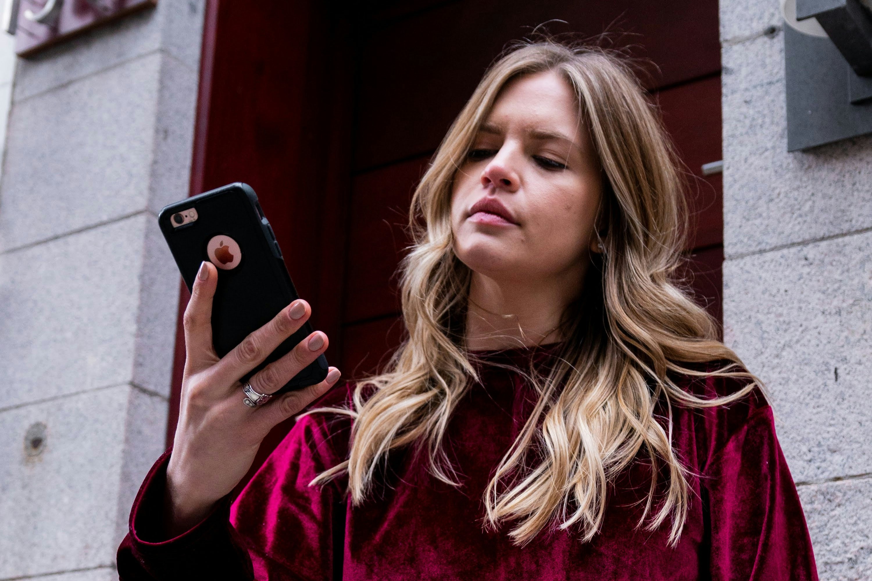 A woman holds her phone up in her hands and looks at it in a slightly vexed way.