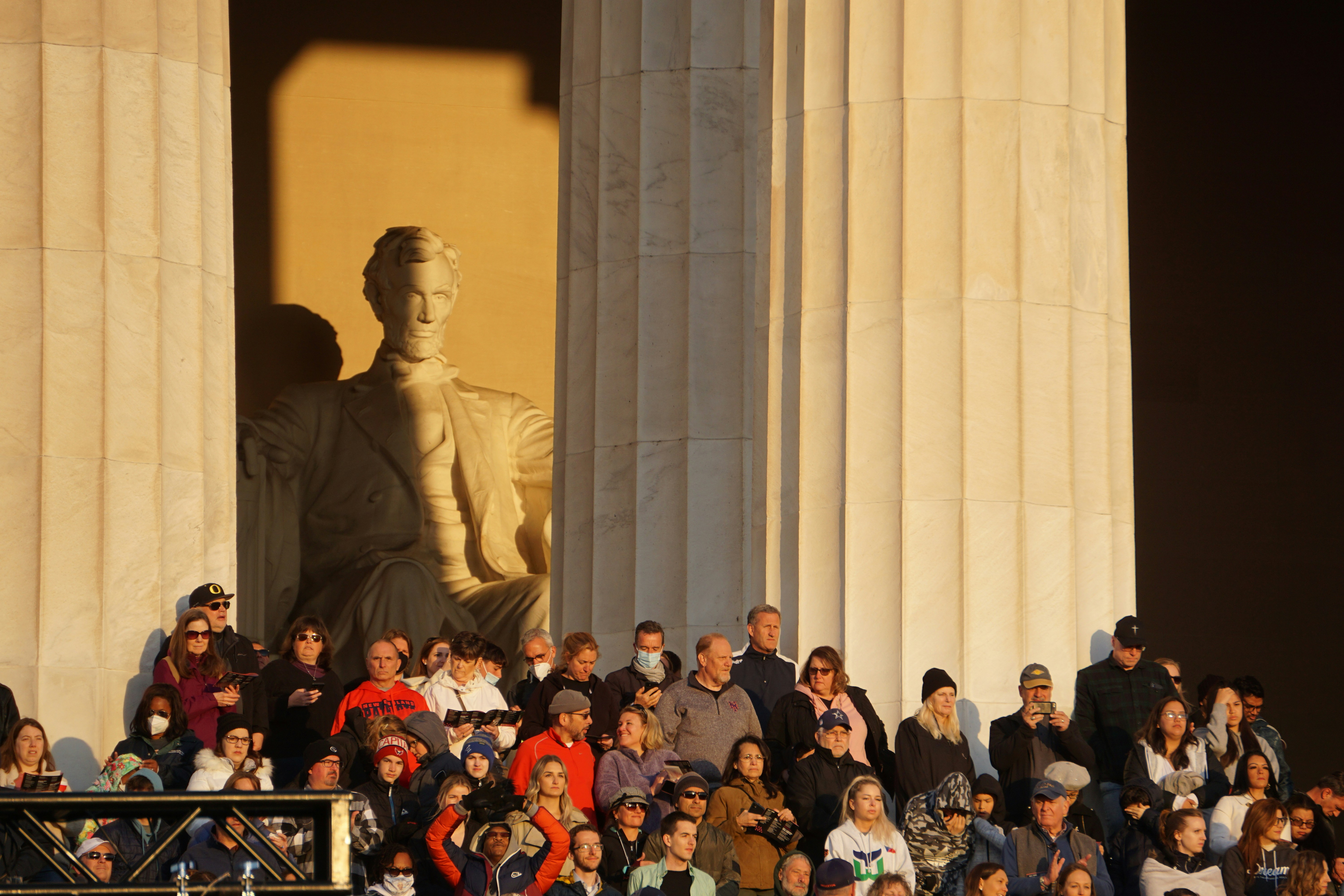 A crowd of people stand in the side steps of the Lincoln Memorial