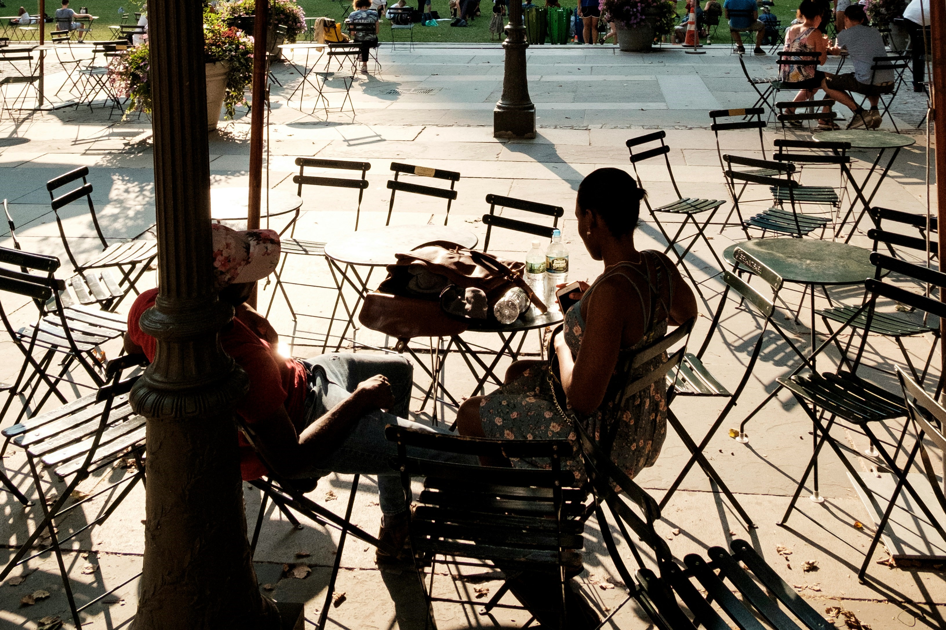 Two people. sitting at a street cafe amid empty tables and chairs, are silhoutted.