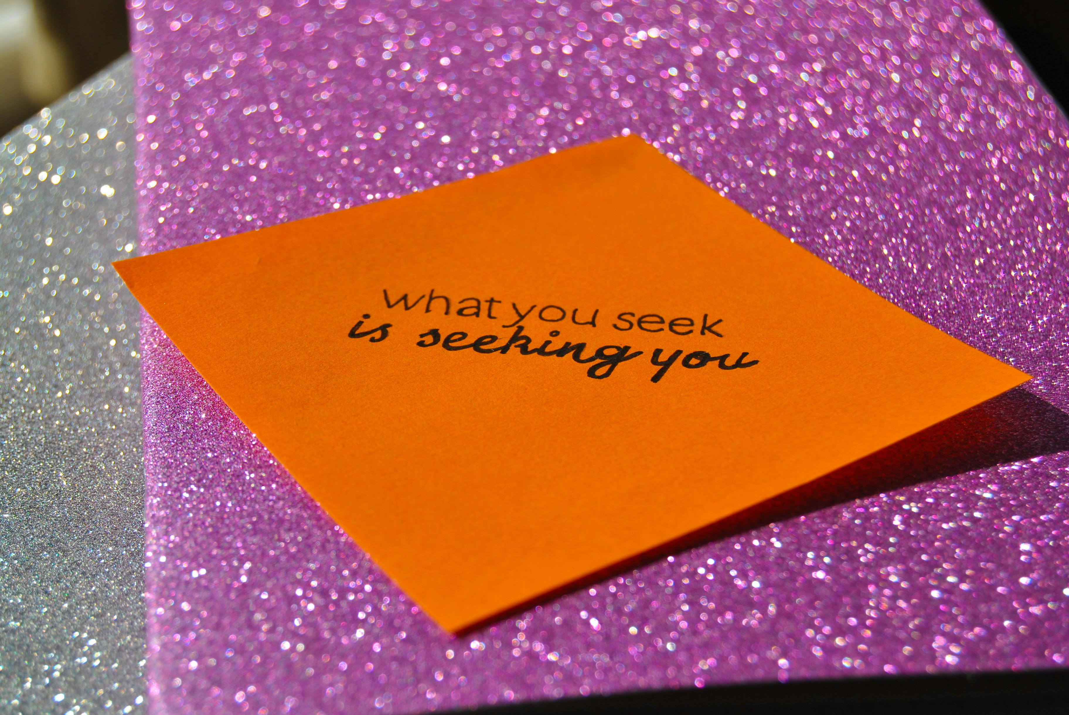 Against a purple glittery background, a orange notelet reads: 'what you seek is seeking you.'