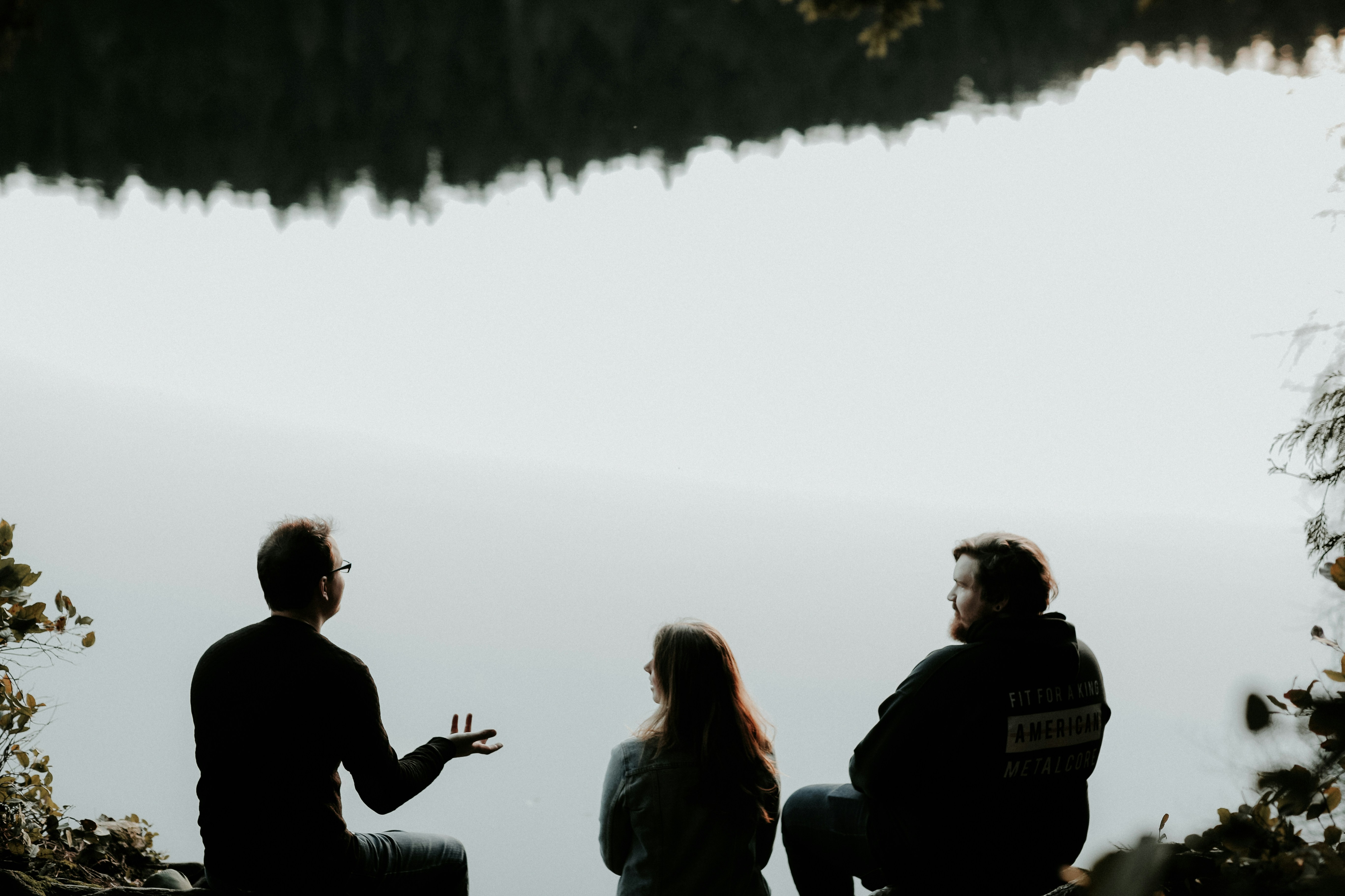 Three people sitting looking out over viewpoint are silhouetted against the sky. 