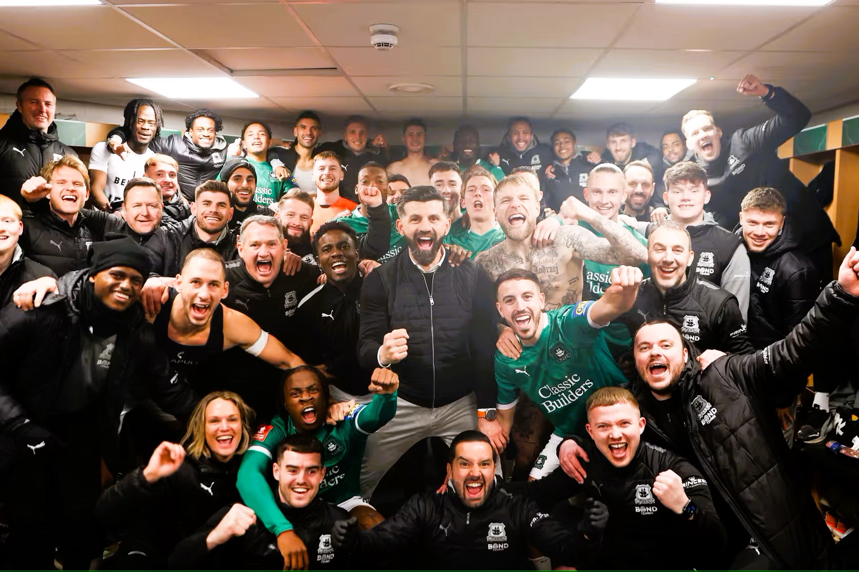 in a dressing room, celebrating footballer crowd together for a photograph.