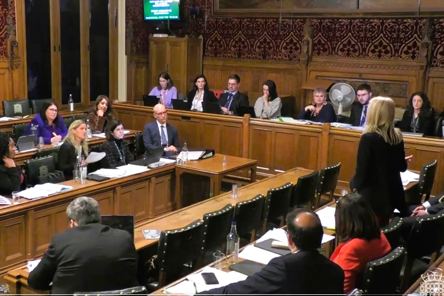 A parliamentary committee meets, sitting at wooden raised desks in a wood panelled room.