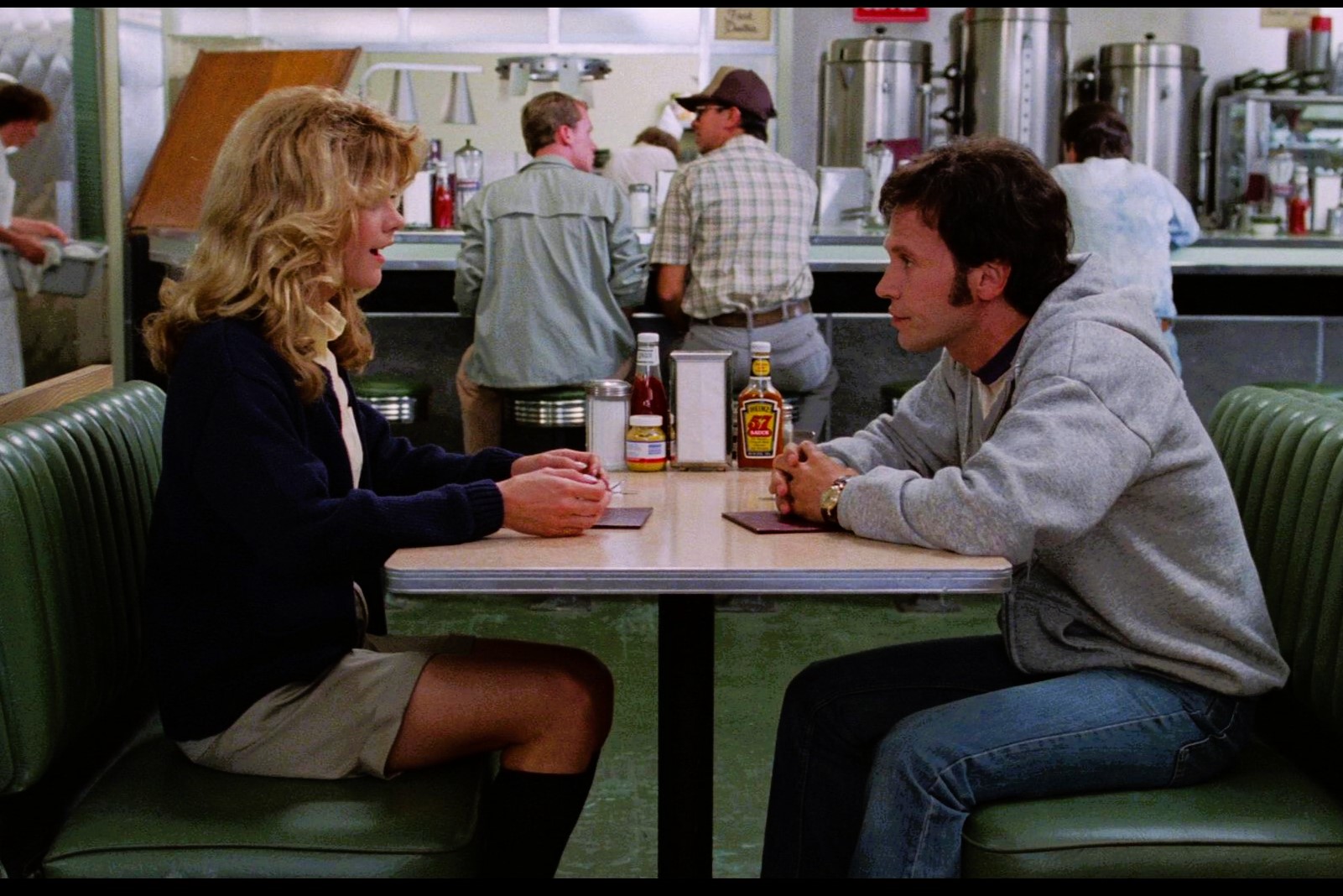 A couple sit at a table in a diner talking intensely.