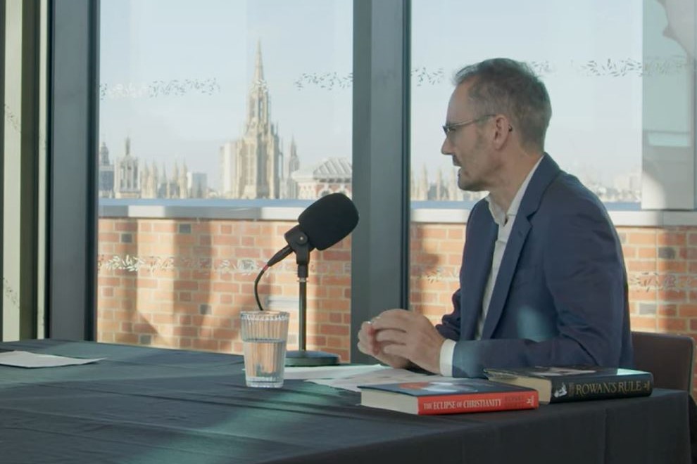 A podcast guest sits at a table in front of a mic. 