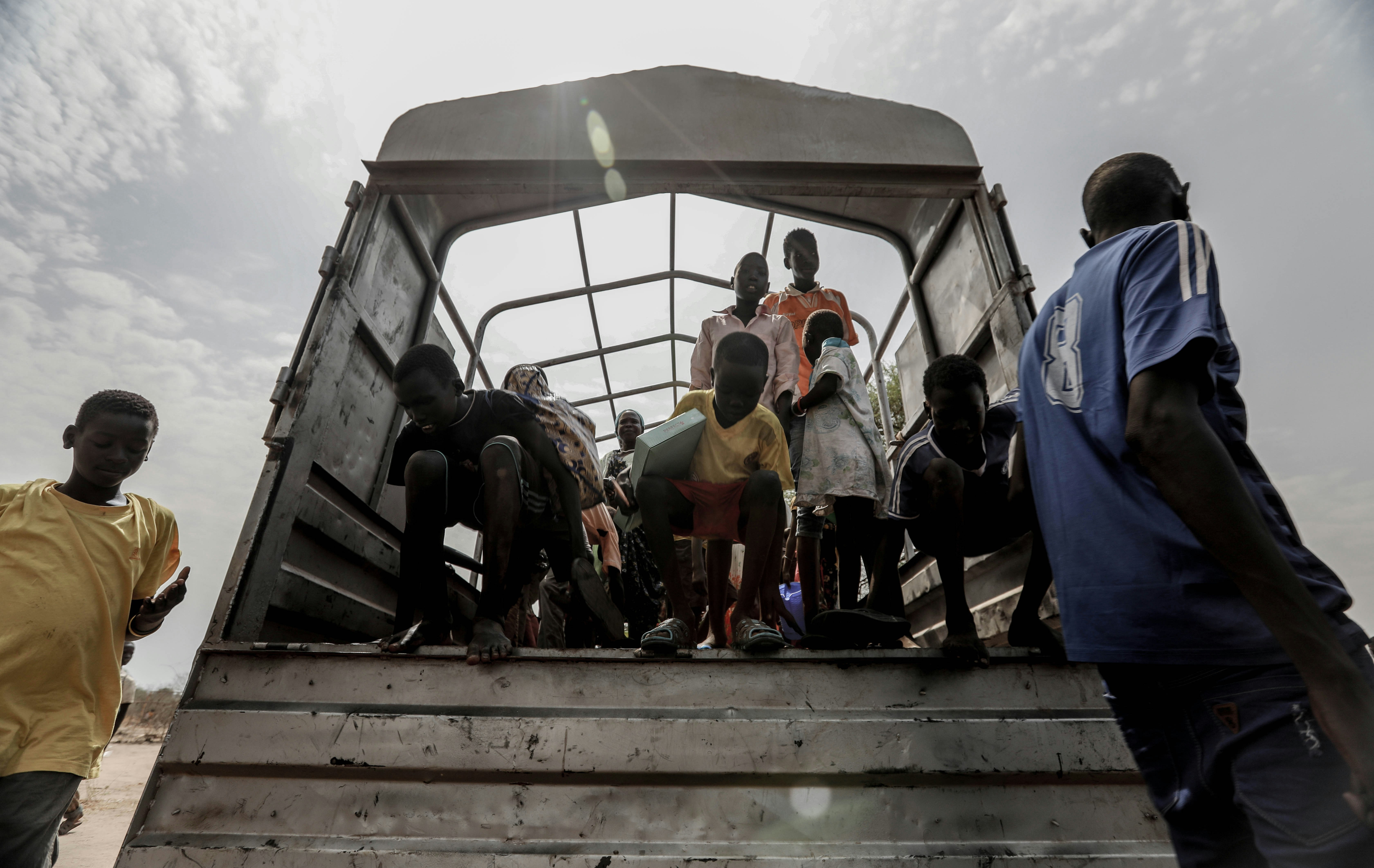 Refugees stand at the back of an open truck.