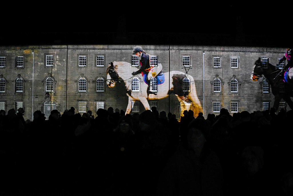 A projection of a horse and rider against a barracks wall.