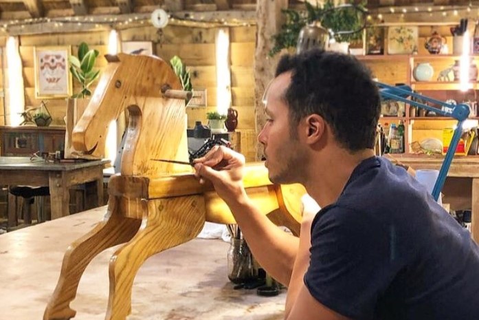 A restorer rest on his elbows while painting a wooden rocking horse.