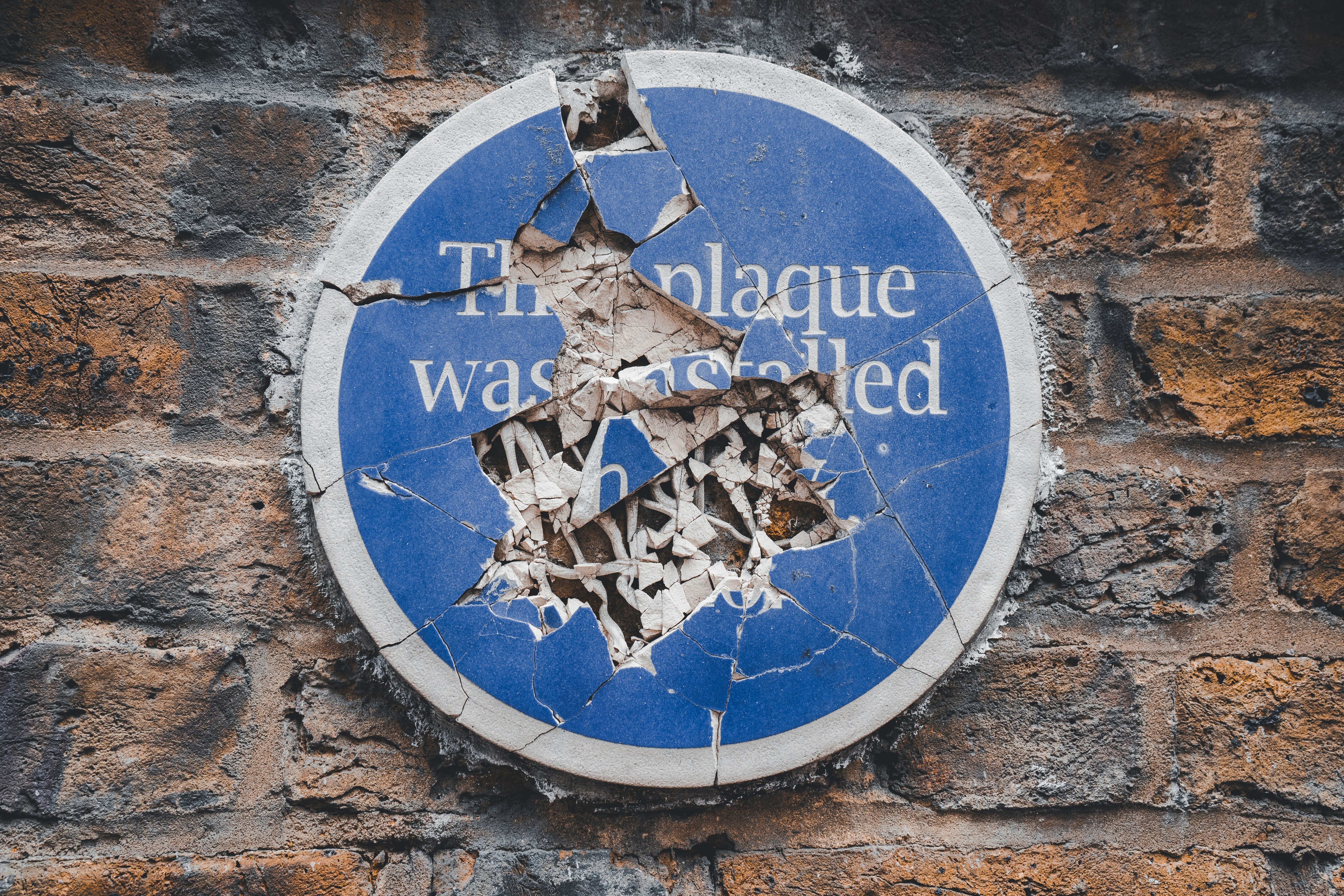 A commemorative blue plaque on a a wall is smashed to pieces