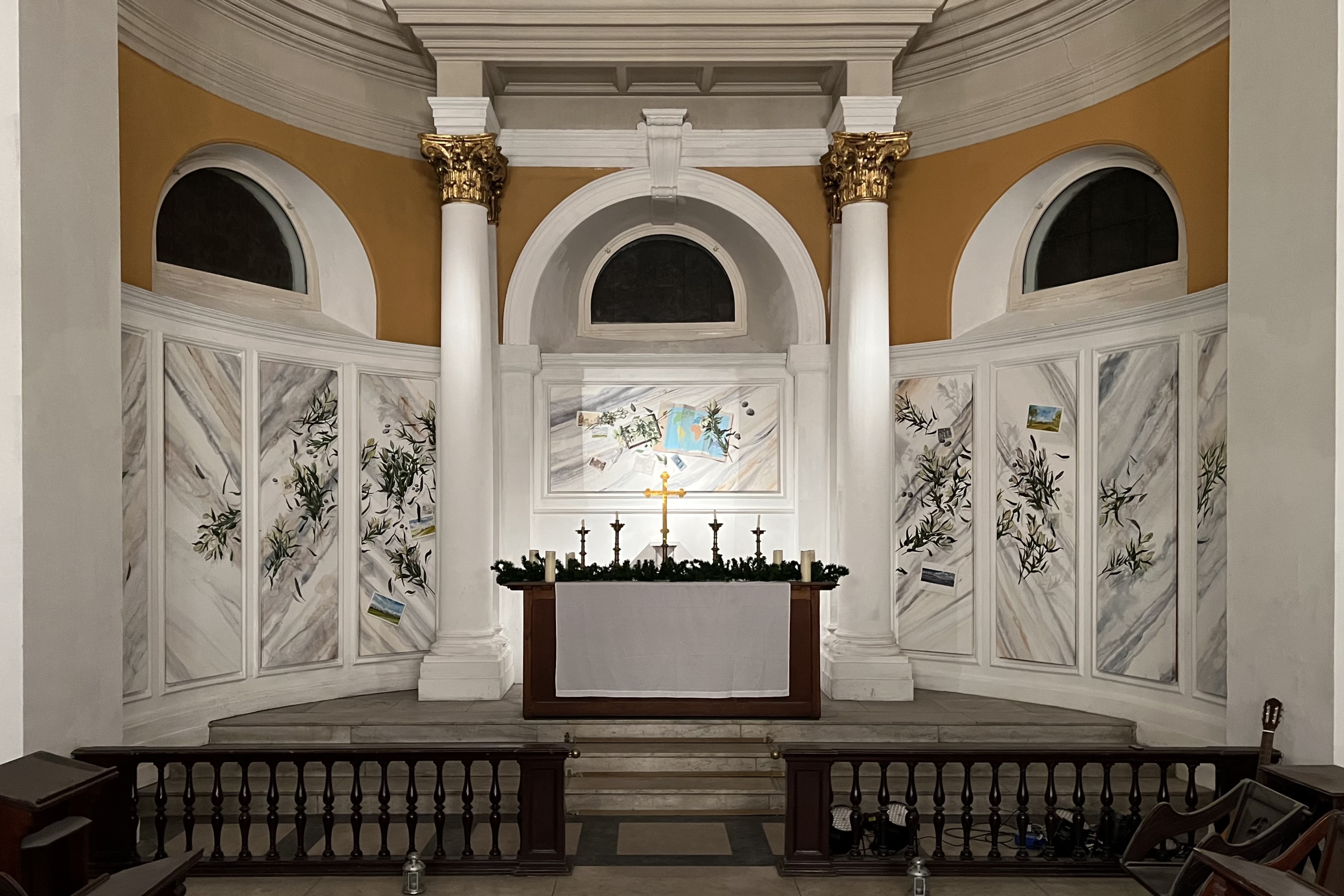 An altar is surrounded behind by a curved wall displaying art work on panels.