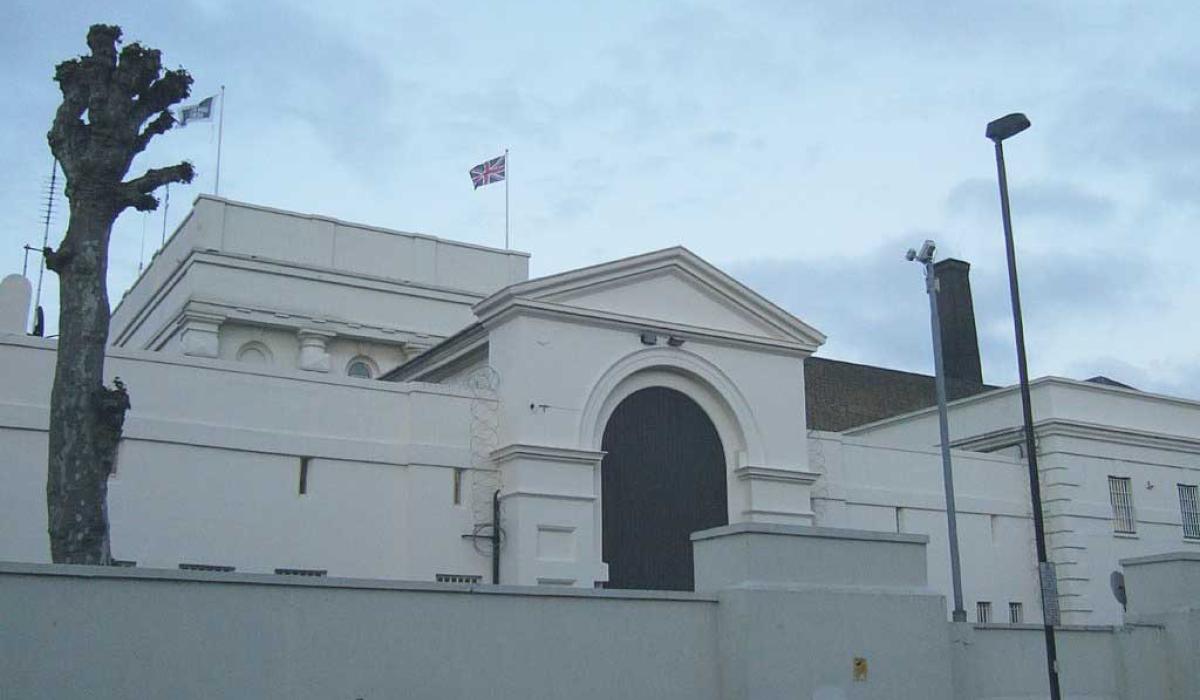 An arched gateway to a prison sits behind a low raised wall. No windows are visible