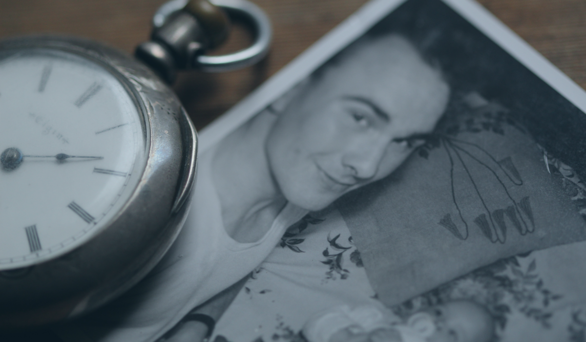 A pocket watch rests next to a black and white photograph of a father lying beside a new born baby.