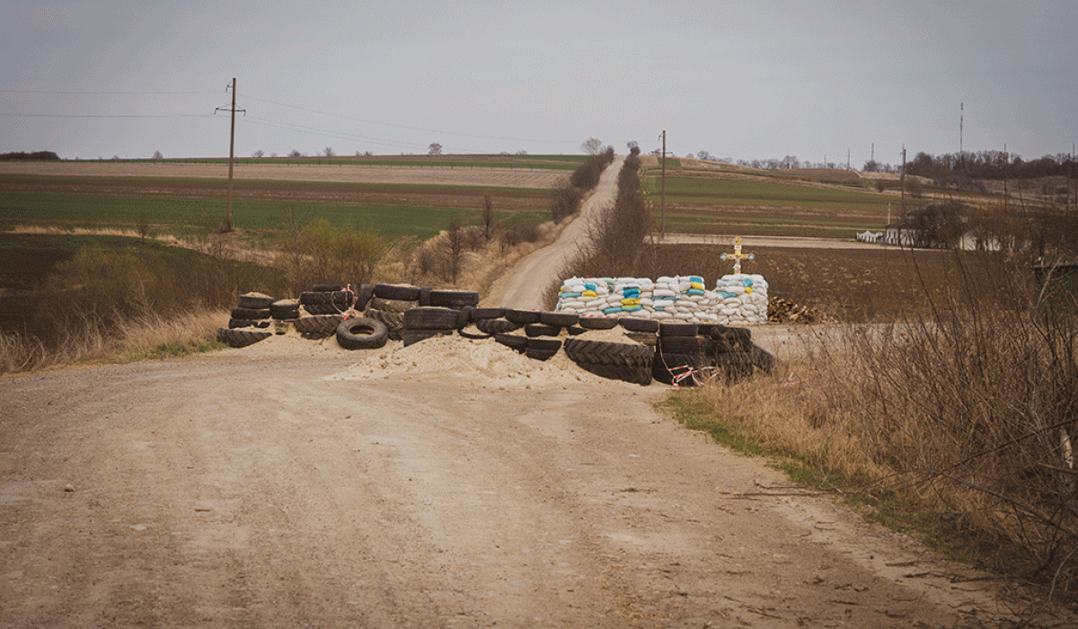 a dirt barricade blocks a cross roads, behind which stands a roadside cross