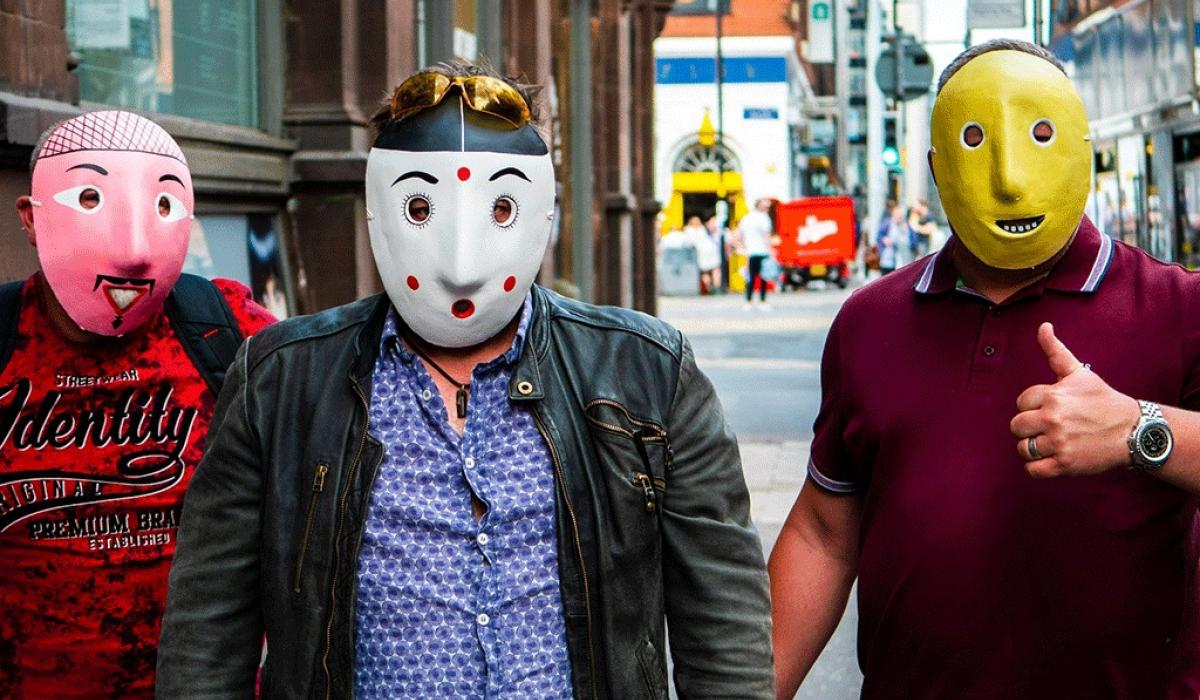 Three men wearing pink, spotty and yellow face masks stand in the street.