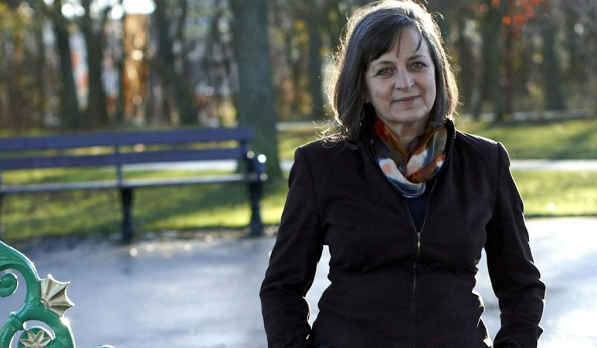 A woman stands in an autumnal-looking park, with her hands in her pockets