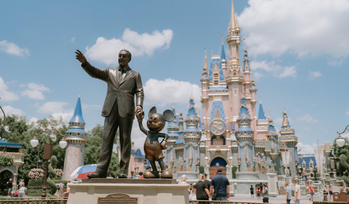 A statue of Walt Disney holding hands with Mickey Mouse in front of Cinderella's Castle