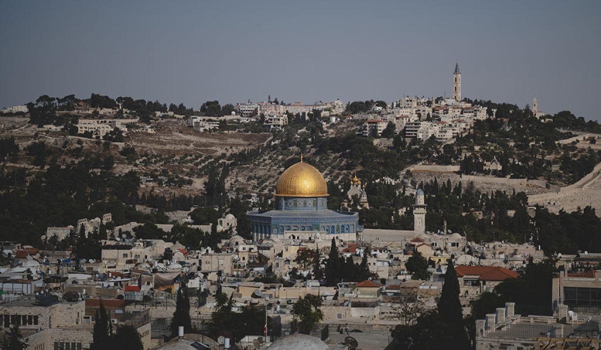 A blue and gold domed mosque sits surrounded by old stone buildings of a city.