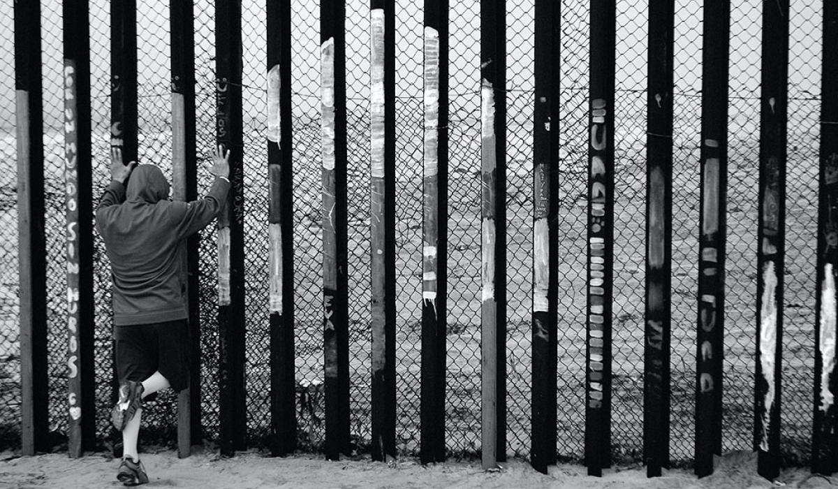 A person holds the vertical tall steel bars of a border fence.