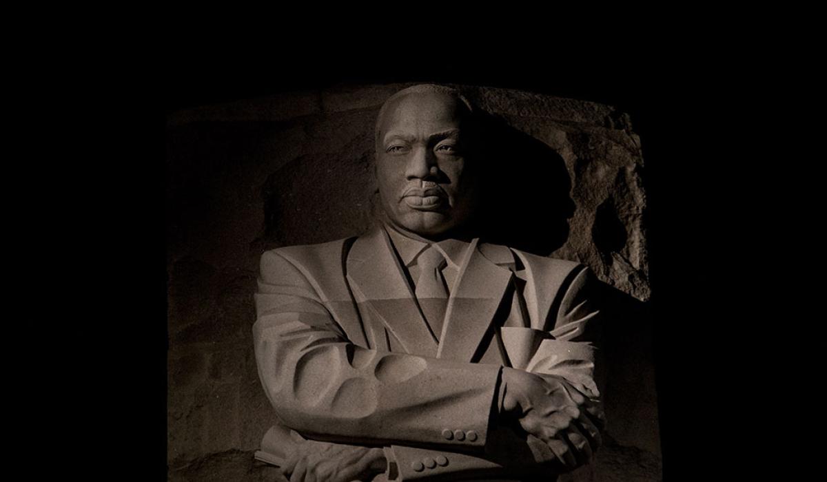 An imposing stone statue of Martin Luther King standing with his arms crossed.