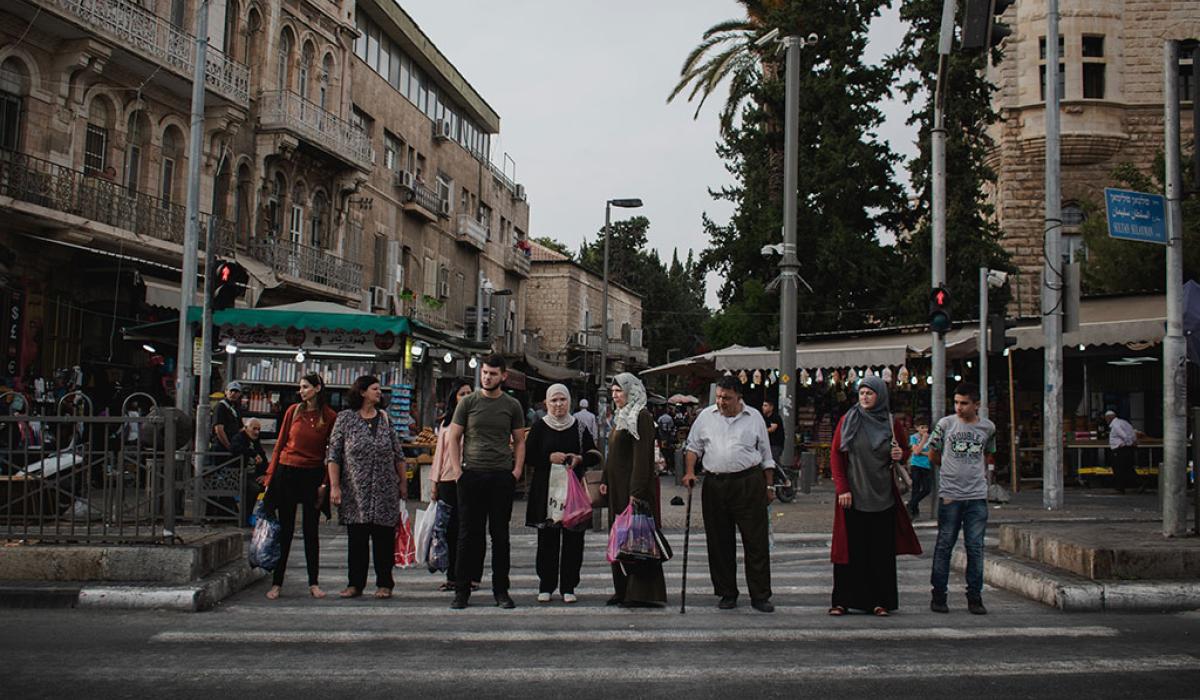 A line of people, some old, some young, wait to cross a road.