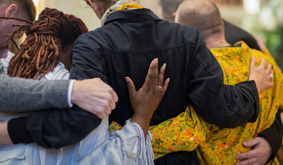 A group of grieving friends with their hands on each others backs.