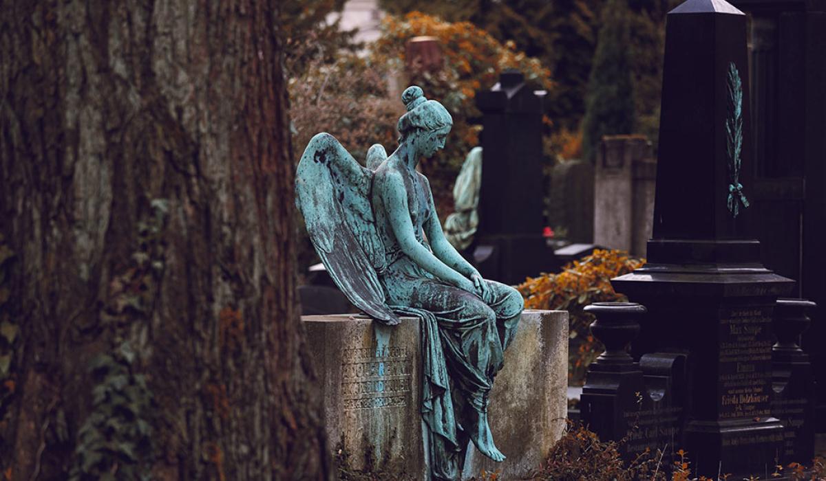 A bronze statue of a resting angel sits atop a low stone grave.