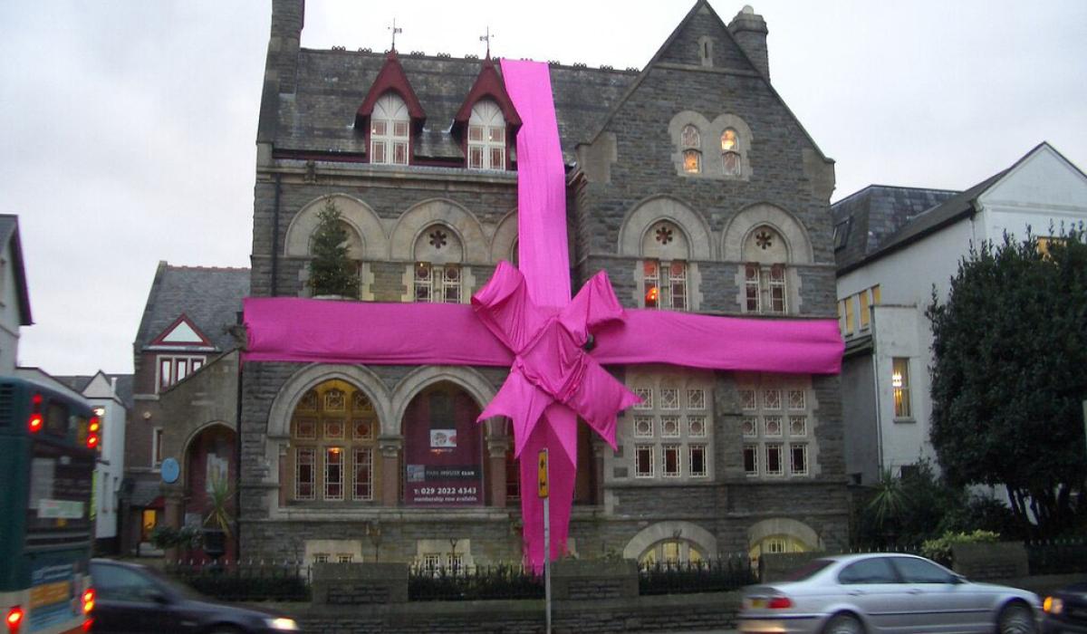 A large stone house is wrapped in a red ribbon and bow.