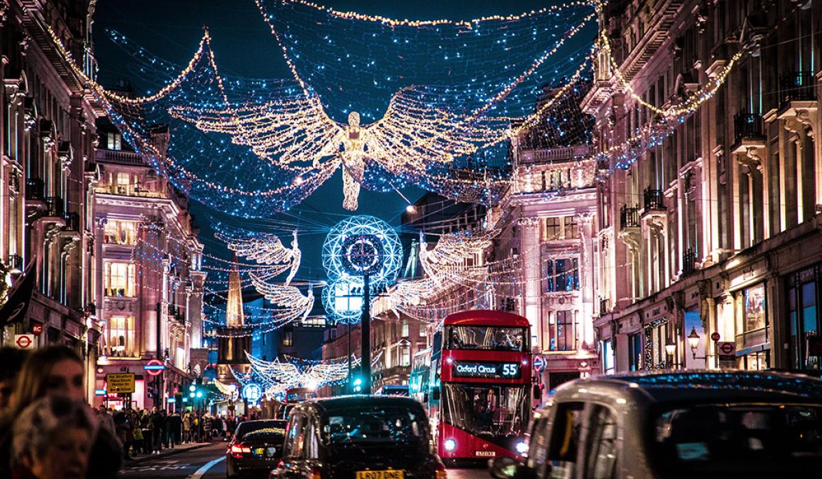 A shopping street is crowded by taxi cabs and buses while above it a Christmas illumination of an angel hangs over all.