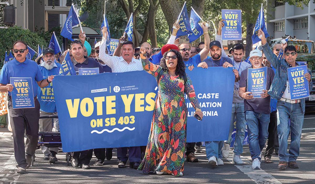 A group of protesters march behind a banner waving flags.