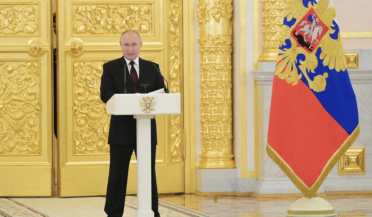 Preisdent Putin stands behind a lectern with a gold door and Russian flag behind him.