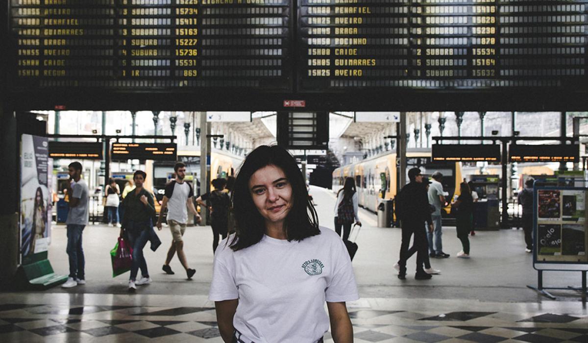 A young person stands in front of railway station platfrorms and below a large informaton display.